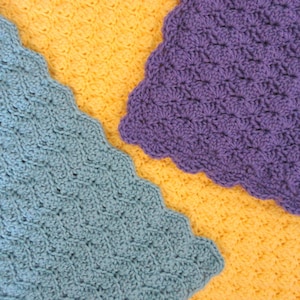 May include: Close-up of three crocheted pieces in shades of yellow, teal, and purple. Each piece has a scalloped edge and a textured stitch pattern. The pieces are arranged diagonally, showcasing the different colors and textures.