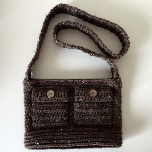 May include: A brown crocheted shoulder bag with two front pockets and two silver buttons.
