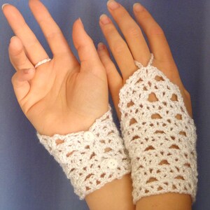 May include: A pair of white crocheted fingerless gloves with button details. The gloves are made with a delicate lace pattern.