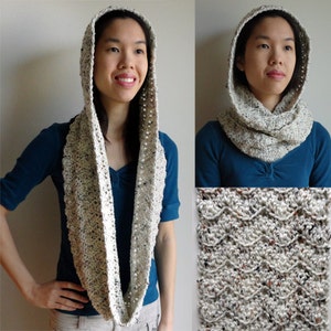 Op de afbeelding: Een witte capuchon-cowl sjaal met een textuurpatroon. De sjaal is gemaakt van een gespikkeld garen en heeft een lang, vloeiend ontwerp.
