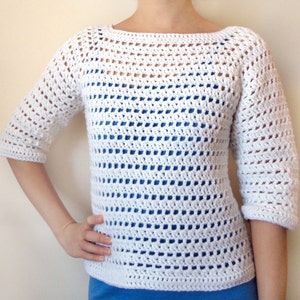 Puede incluir: Top blanco de crochet con un ajuste holgado y mangas 3/4. El top tiene un escote amplio y abierto y un delicado patrón de punto abierto.