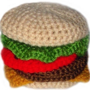 Könnte beinhalten: Ein gehäkeltes Hamburger-Spielzeug mit einem beigen Brötchen, grünem Salat, roter Tomate, braunem Patty und gelbem Käse.