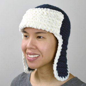May include: A navy blue crocheted hat with white ear flaps and a white crocheted brim.