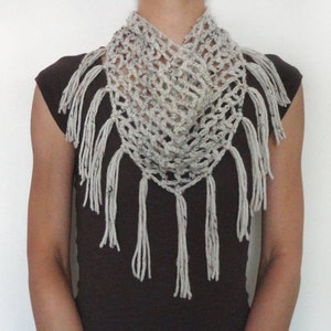 Pode incluir: Uma echarpe branca de crochê com franjas. A echarpe é feita com um padrão delicado de ponto aberto.