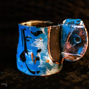 Könnte beinhalten: Handbemalte Keramiktasse mit blauem, schwarzem und weißem abstraktem Design. Die Tasse hat einen einzigartigen Griff und ist mit Pinselstrichen und Spritzern verziert. Ein einzigartiges Kunstwerk.