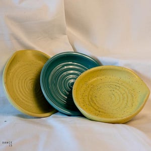 Può includere: Tre piatti in ceramica, uno blu-verde e due gialli con macchie. I piatti hanno un motivo a spirale e sono perfetti per servire piccoli spuntini o salse.