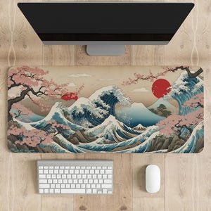 Puede incluir: Una alfombrilla de escritorio grande con un diseño de inspiración japonesa que presenta una gran ola, un sol rojo y flores de cerezo. La alfombrilla es beige con acentos azules, blancos y rojos.