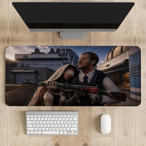 May include: A rectangular desk mat featuring a graphic illustration of two figures with covered eyes standing before the Cedar Creek Nuclear Power Plant. One figure holds a rifle decorated with red floral patterns, while the other wears a textured shawl.