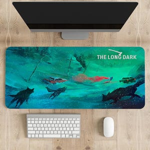 Puede incluir: Un tapete de ratón para juegos azul y verde con un paisaje nevado y el texto "THE LONG DARK" en blanco. La imagen presenta una figura solitaria en la distancia, un coche estrellado y lobos en primer plano.