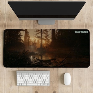 Pode incluir: Um tapete de rato para jogos de cor castanho escuro com uma cena de floresta e um rio em primeiro plano. O texto "ALAN WAKE II" está no canto superior direito.