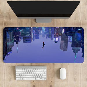 May include: A desk mat with a city skyline upside down, a person in a red and black suit is falling from the sky. The mat is on a wooden surface with a computer monitor, keyboard, and mouse.