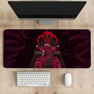 Puede incluir: Un tapete de ratón para juegos rojo y negro con un gráfico de un monstruo rojo con tentáculos y una pirámide roja con un símbolo en la parte superior. El tapete de ratón está sobre una superficie de madera con un monitor de computadora, un teclado y un ratón.