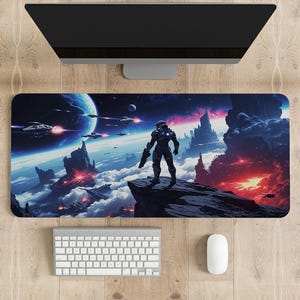 Puede incluir: Una alfombrilla de escritorio rectangular con una ilustración de ciencia ficción de una figura con traje espacial sobre un acantilado rocoso, observando un planeta, nubes y naves espaciales frente a una nebulosa y un horizonte rojo.