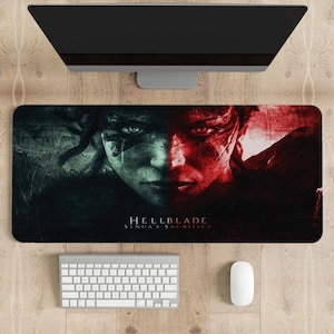 May include: A black gaming mouse pad with a graphic of a woman's face split in half, one side green and the other red. The text "Hellblade: Senua's Sacrifice" is printed in white at the bottom.