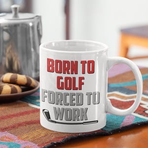 May include: White ceramic coffee mug with a black and gray golf club graphic and the text "Born to Golf Forced to Work" in red and gray lettering.