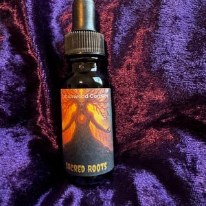Può includere: Una bottiglia di vetro scuro con contagocce. L'etichetta recita "Cottonwood Conjure" sopra un'illustrazione di una figura a forma di albero. Le parole "Sacred Roots" sono sotto. La bottiglia è su una superficie di velluto viola.