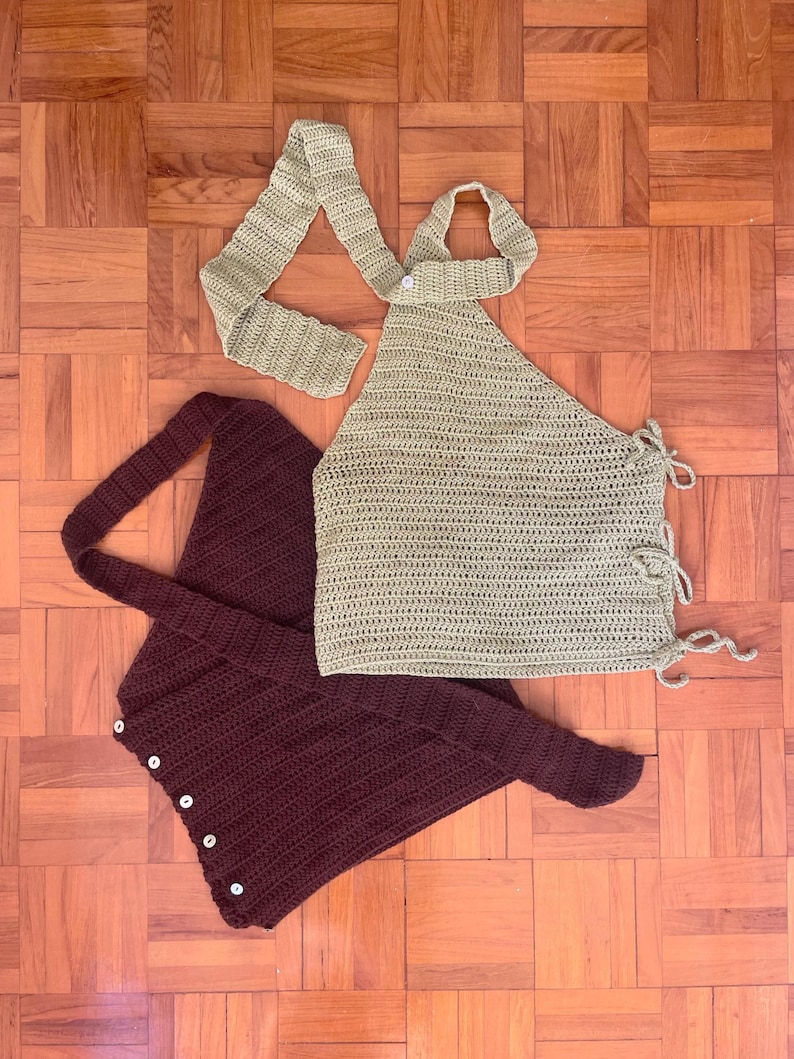 May include: Two handmade crochet tops in the image. One is a light olive green halter top with tie closures. The other is a deep burgundy wrap top with button closures. Both tops are made of a textured yarn and are displayed on a wooden surface.