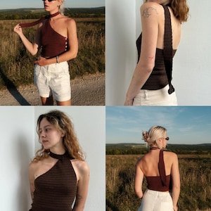 May include: A dark brown, one-shoulder top with a halter neck and button details. The top is paired with white shorts. The image is taken outdoors with a field and blue sky in the background. The top has a unique design.
