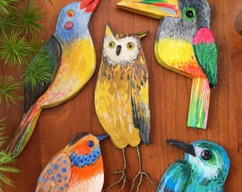 May include: Five hand-painted wooden bird ornaments. The birds are a toucan, an owl, a blue bird, a robin, and a yellow bird. The birds are all different sizes and shapes.