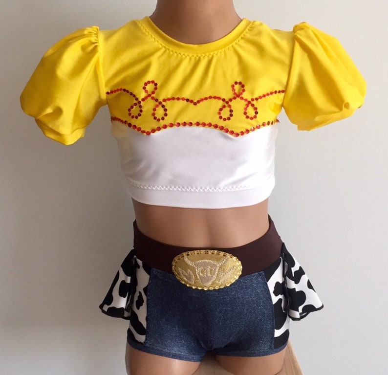 May include: A yellow and white crop top with a red and white design and a brown belt with a gold buckle. The top has short puffed sleeves. The belt has a cow print design. The outfit is a costume for a character from the movie Toy Story.