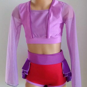Op de afbeelding: Een danskostuumset in paarse en rode tinten. De set bevat een crop top met lange, doorschijnende mouwen, een broek met hoge taille en een ruches accent, en bijpassende shorts. De outfit is ontworpen voor dans of optredens.