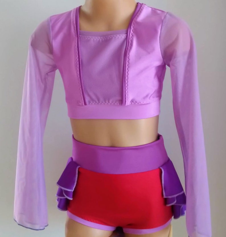 Op de afbeelding: Een danskostuumset in paarse en rode tinten. De set bevat een crop top met lange, doorschijnende mouwen, een broek met hoge taille en een ruches accent, en bijpassende shorts. De outfit is ontworpen voor dans of optredens.