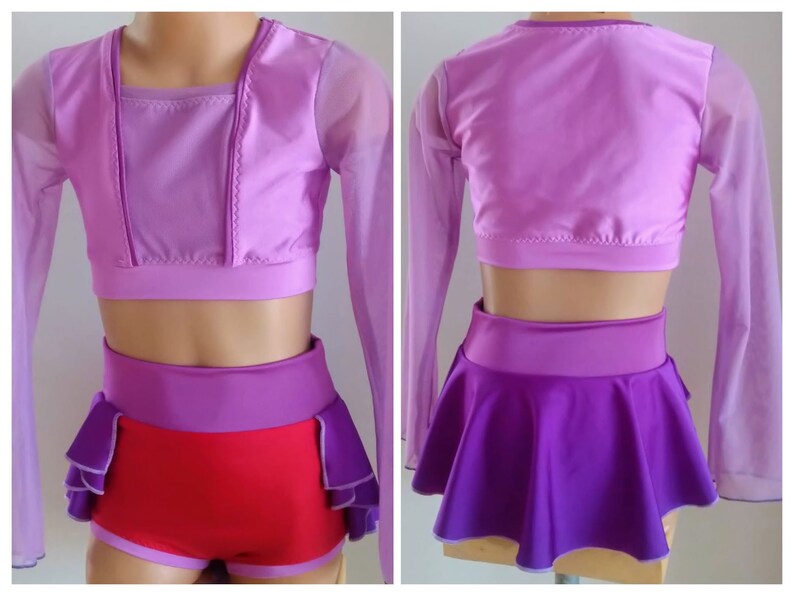 Op de afbeelding: Een tweedelig danskostuum in paarse en rode tinten. De top is een cropped ontwerp met lange mouwen en een vierkante halslijn. De shorts zijn rood met paarse accenten en de rok is paars. Het kostuum is ontworpen voor dans of optredens.