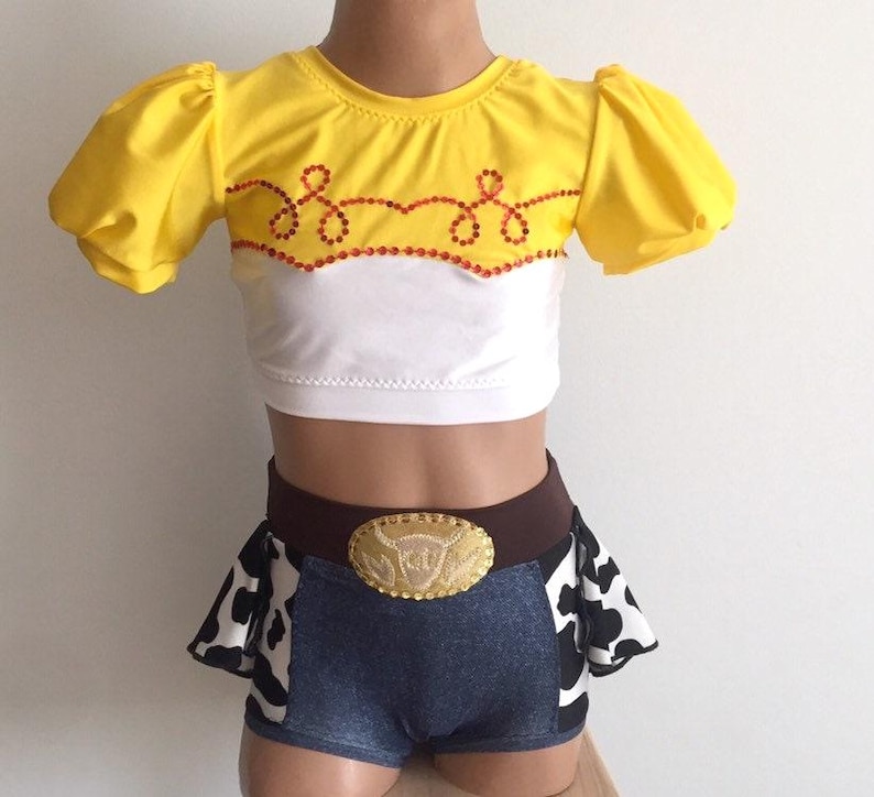 May include: A yellow and white crop top with a red and white trim and a cow print skirt with a brown belt and a gold buckle. The belt buckle has a cow head design.
