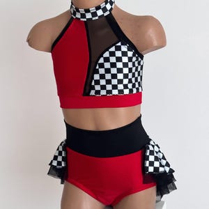 May include: A two-piece dance costume in red, black, and white. The top has a halter neck with a checkered pattern, red panels, and a mesh insert. The high-waisted bottoms are red with a black waistband and checkered accents.