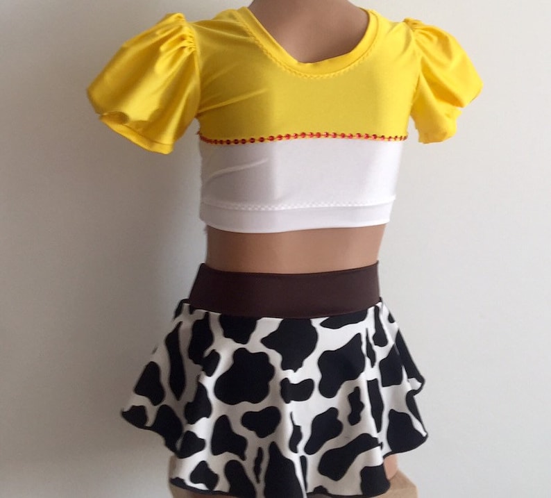May include: A two-piece costume for a child, featuring a yellow and white top with puffed sleeves and a black and white cow print skirt with a brown waistband.