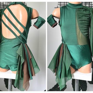 May include: A green leotard with a sheer overlay and a criss-cross back design. The leotard has a brown ruffle trim and a long sheer sleeve on one side.