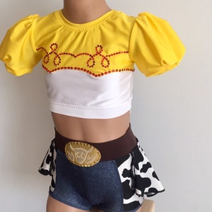 May include: A yellow and white crop top with a red and white design and a denim skirt with a cow print and a brown belt with a gold buckle. The outfit is inspired by a popular cartoon character.