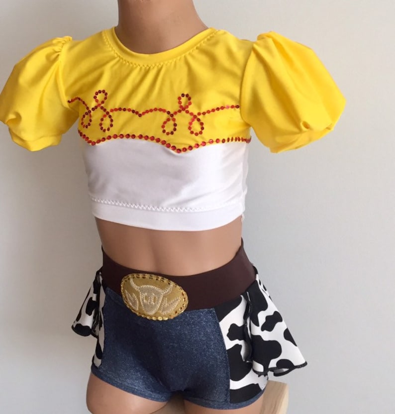 May include: A yellow and white crop top with a red and white design and a denim skirt with a cow print and a brown belt with a gold buckle. The outfit is inspired by a popular cartoon character.