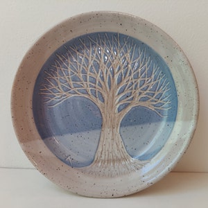 May include: A ceramic plate with a white tree design on a blue background. The plate has a speckled white glaze.
