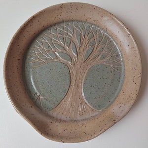 May include: A ceramic dish with a tree of life design in brown and green. The dish has a speckled glaze and a brown rim.