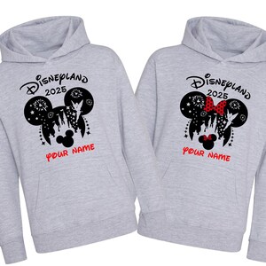 Może przedstawiać: Dwie szare bluzy z kapturem z czarno-białym nadrukiem głowy Myszki Miki z tekstem "Disneyland 2025" i "Your Name" nadrukowanym z przodu.