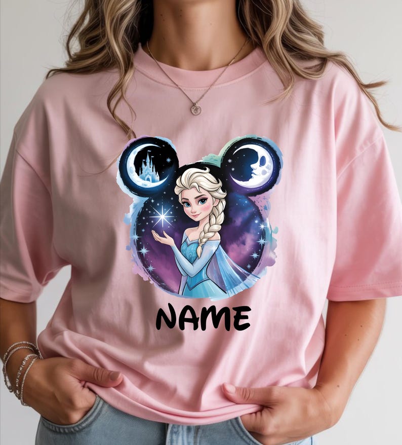 May include: Light pink t-shirt featuring a graphic of a princess with a blue dress and a braided hairstyle. The design includes a starry background, a castle, and the word "NAME" in black.