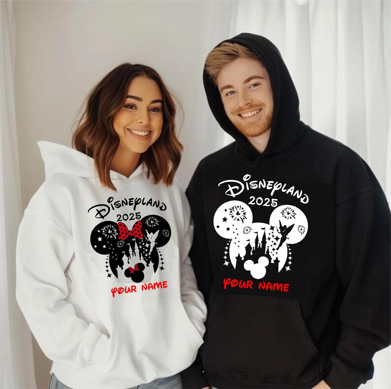 Może przedstawiać: Biała i czarna bluza z nadrukiem w kształcie uszu Myszki Miki. Nadruk zawiera sylwetkę zamku Kopciuszka, fajerwerki, Dzwoneczek i napis "Disneyland 2025". Pod nadrukiem znajduje się napis "Your Name".