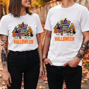 May include: White t-shirts featuring a colorful graphic print of various Halloween characters, including a stack of VHS tapes, pumpkins, and a black cat. The word HALLOWEEN is printed in orange, dripping-style letters at the bottom of the graphic.