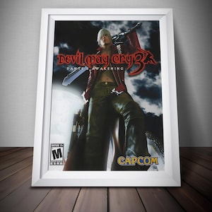 May include: Framed poster for the video game "Devil May Cry 3: Dante's Awakening." The artwork features a character with white hair, a red jacket, and a sword. The ESRB rating is visible. The Capcom logo is at the bottom.