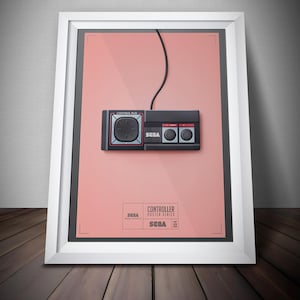 May include: Framed poster featuring a black Sega Genesis controller on a pink background. The controller has a directional pad, two buttons, and the Sega logo. The poster is part of the "Controller Poster Series" and is framed in a white frame.