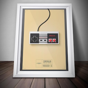 May include: Framed poster featuring a classic Nintendo controller design. The controller is white, black, and red, with the Nintendo logo. The poster is part of the "Controller Poster Series" and is framed in a white frame.