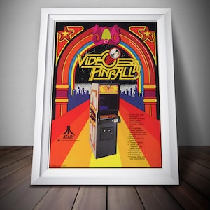 May include: Framed vintage Atari "Video Pinball" arcade game poster. The poster features a colorful design with a retro aesthetic, including a pinball machine illustration and the game's title. The poster is framed in a white wooden frame.