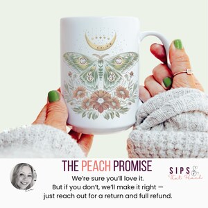 May include: White ceramic mug featuring a green and gold moth design with a crescent moon and floral accents. The mug has a large handle and is held by a person. The text "THE PEACH PROMISE" is visible.