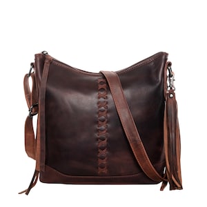 May include: A dark brown leather crossbody bag with a long adjustable strap. The bag features a decorative stitched design down the center and a tassel on the side. The bag has a zipper closure and a small handle.