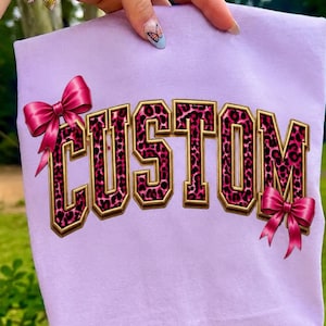 Nome personalizzato con stampa leopardata rosa in formato PNG, lettere personalizzate con fiocco stile college, design personalizzato per sublimazione del testo, download digitale in formato PNG per maglietta Coquette.