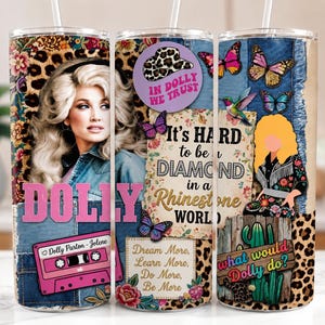 May include: A cylindrical tumbler featuring a collage of Dolly Parton imagery, including a portrait, a pink cassette tape labeled Dolly Parton-Jolene, butterflies, leopard print, denim textures, and text reading In Dolly We Trust and It's Hard to be a Diamond in a Rhinestone World.
