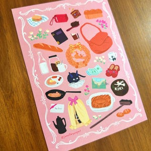 Pu&ograve; includere: Una cartolina rosa con illustrazioni di vari oggetti, tra cui cibo come pane, pancake e una pagnotta, insieme a una borsa, un libro e un gatto. La cartolina ha un bordo decorativo bianco e il testo "@jenniferyangart".