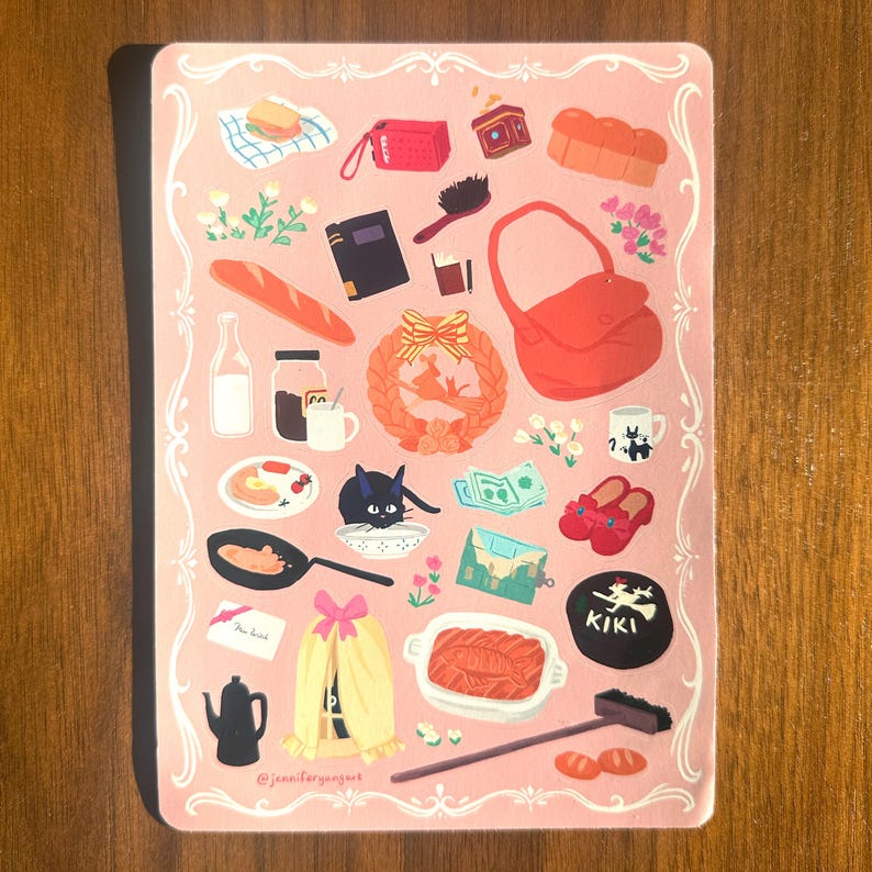 Pu&ograve; includere: Illustrazione rosa con cornice decorativa, raffigurante vari oggetti, tra cui una borsa rossa, un gatto nero e una baguette. L'illustrazione include il testo "KIKI" e "@jennifergangkuk".