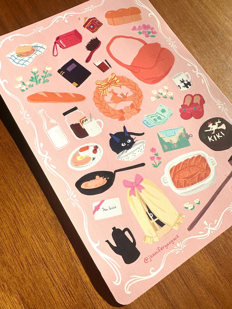 Pu&ograve; includere: Un foglio di adesivi rosa con illustrazioni di un gatto nero, una teiera, una borsa e cibi come pane e un uovo fritto. Il foglio ha un bordo decorativo e il testo "New Witch".